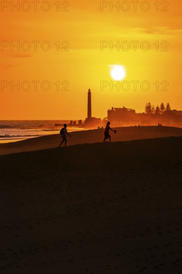 Tourists walking on the maspalomas dunes at sunset, with the maspalomas lighthouse in the