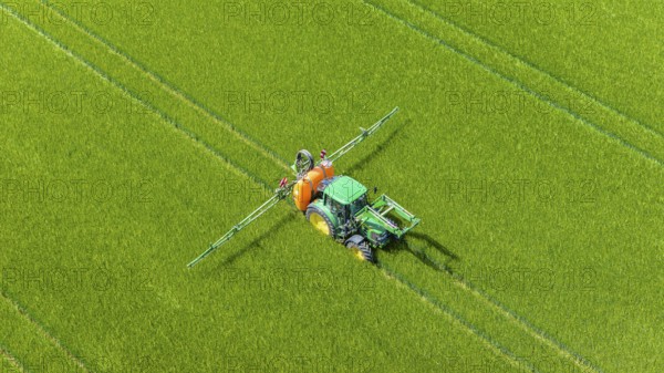 Farmer with tractor working in the field. In early summer, he fertilises the grain for an optimum