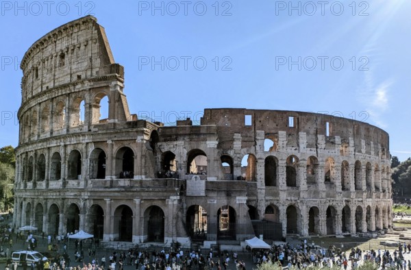 Side view of the Colosseum with tourists visible and sunlight illuminating its arches. Rome, Italy
