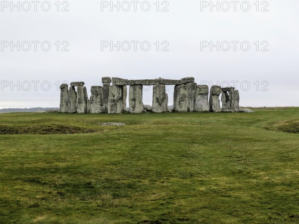 Distant view of Stonehenge surrounded by green grass under an overcast sky. Salisbury, England,