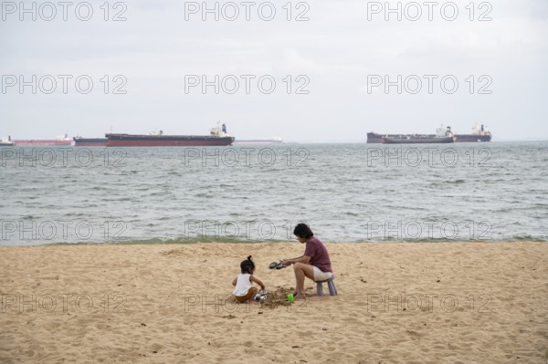 31.07.2023, Singapore, Republic of Singapore, Asia, A woman and a small child sit in the sand on