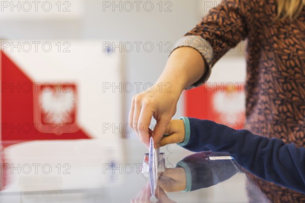 Woman's and kid's hands puting a card with a vote to the ballot box during parliamentary elections.