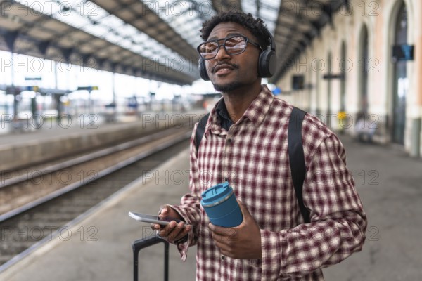Traveler with headphones and backpack holding smartphone and reusable coffee cup is waiting for