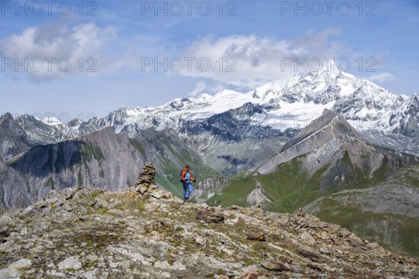 Female mountaineer on hiking trail with cairn, behind glaciated and snow-covered summit of the