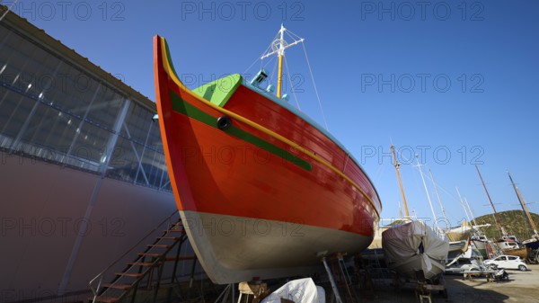 Side view of an orange-coloured boat in a shipyard under a blue sky, Diakofti boatyard, new