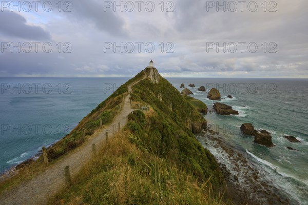 A lighthouse on narrow cliffs overlooking the sea under a cloudy sky, summer, Nugget Point
