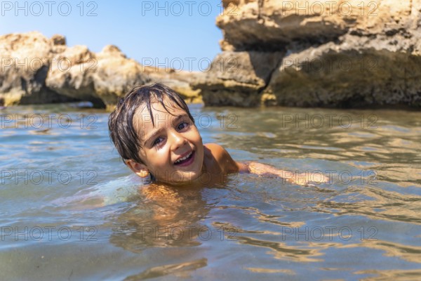 Young boy enjoying a refreshing swim in the ocean, surrounded by beautiful rock formations on a