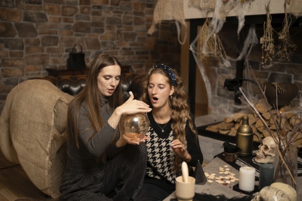 Two women sit on a cozy floor, focused on a swirling crystal ball amidst a warm, inviting
