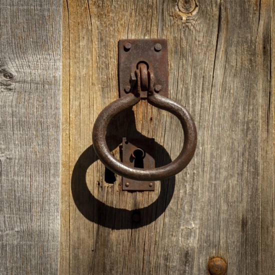 A weathered wooden door showcases an ornate metal knocker and an antique keyhole, reflecting the