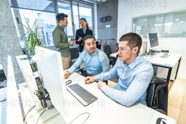 Two customer service representatives working on computer in a busy call center, assisted by their