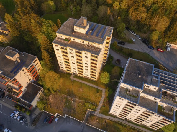 Residential complexes surrounded by trees, with cars in car parks, bathed in warm evening light,