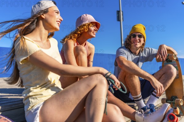 Three happy friends enjoying a sunny day at the beach, sitting on a wooden pier, talking and