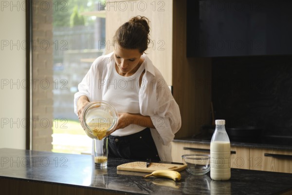 A person blends banana and sea buckthorn in a cozy kitchen. Ingredients are prepared on the