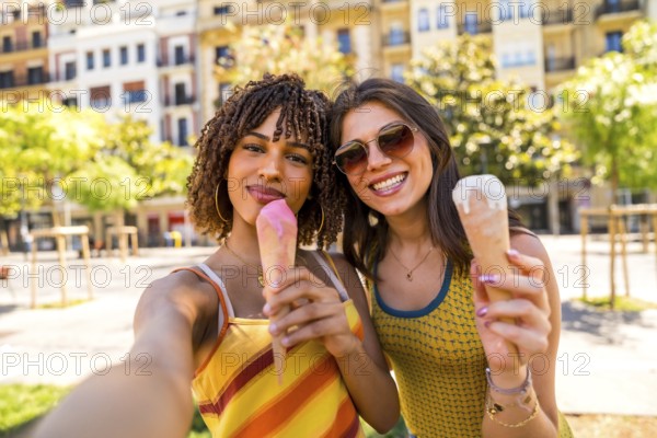 Two happy female friends enjoying ice cream cones on a sunny day in the city, taking a selfie to