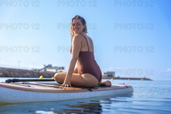 Smiling woman sitting on a paddleboard in calm blue waters, enjoying a sunny summer day at the