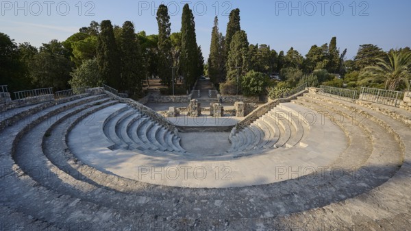 Ancient amphitheatre with rows of stone seats and large trees in the background, Ancient Theatre,
