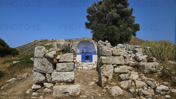 Stone chapel with blue façade amidst ancient ruins, embedded in lush vegetation, Artemis Temple,