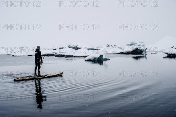 Man stand up paddling, snowfall, glacial lake Jökulsarlon at Vatnajökull, Iceland* Man stand up