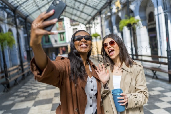 Two cheerful businesswomen taking a selfie with a smartphone and waving at the camera while walking