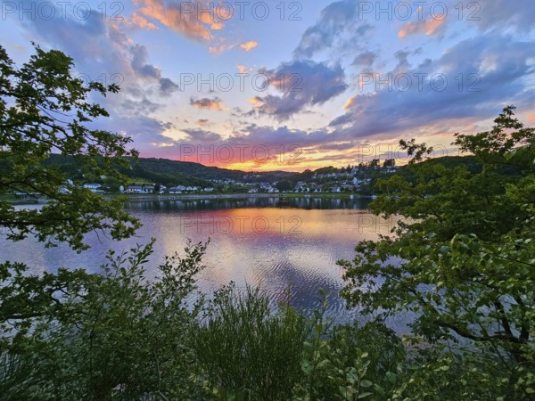 Colourful sunset over a calm lake, surrounded by trees and reflecting clouds in the sky, summer,
