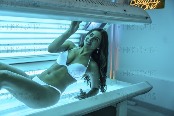 Young woman smiling while enjoying the warmth of a tanning bed, soaking up uv light for a