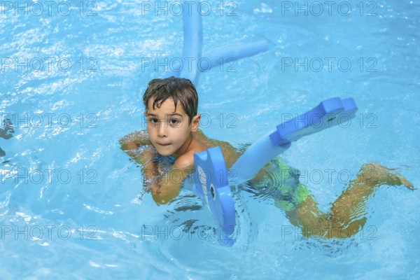 Young boy enjoying summer days, playing with a blue floating toy in a refreshing blue pool under