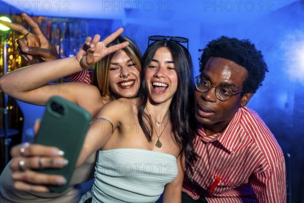 Happy multi ethnic friends taking a selfie while partying in a nightclub, making peace signs and