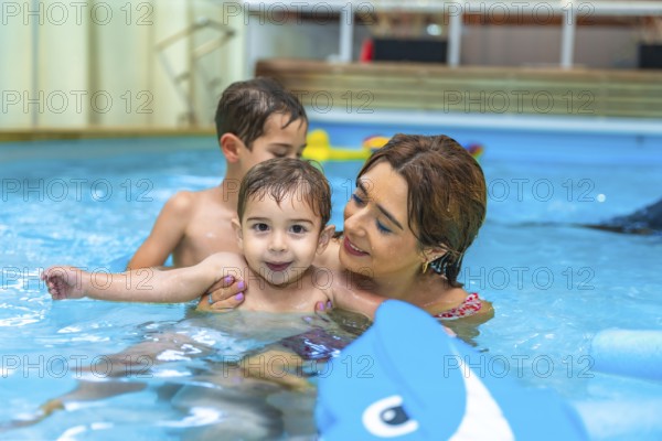 Mother and two sons enjoying time together, playing with inflatable toy in home swimming pool,