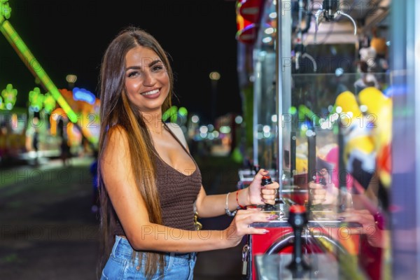Happy young woman enjoying playing a claw crane game at an amusement park, trying to grab a prize