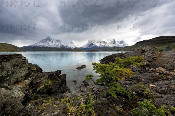Cloudy mountain range Cuernos del Paine, shore of the blue lake Lago Pehoe in the evening light,
