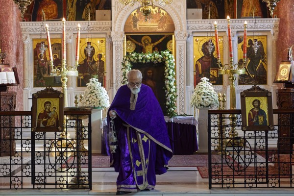 Priest in purple robe walking past an altar with icons and burning candles, Church of the