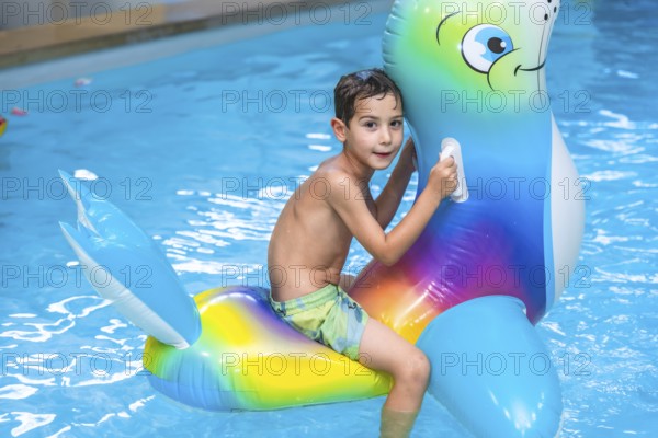 Smiling boy riding a colorful inflatable sea lion toy while splashing in the swimming pool during a