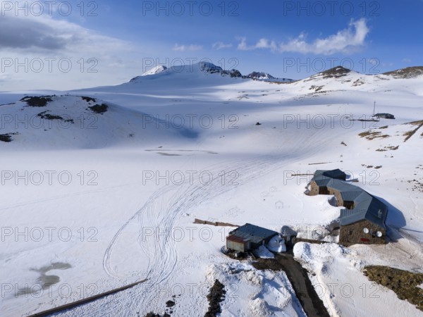Snow-covered huts lie in a peaceful mountain landscape under a blue sky, aerial view, Aragaz,