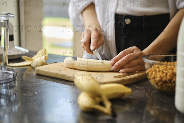 In a warm kitchen, a person slices ripe bananas on a wooden cutting board. Fresh sea buckthorn
