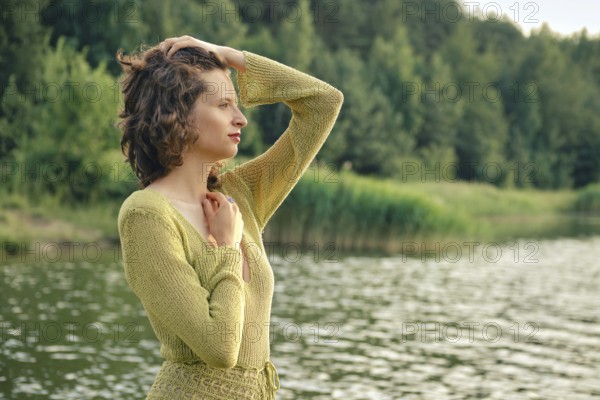 On a hot summer day, a woman stands by the tranquil lake, her hand resting on her head while she