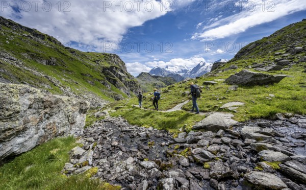 Mountaineers on a hiking trail along a mountain stream in a mountain landscape, descent at Col du