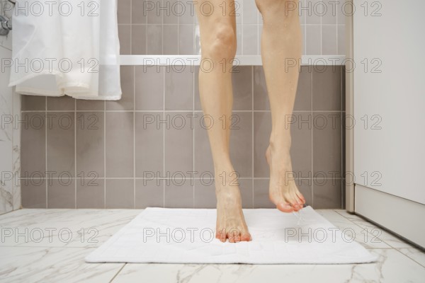 A person is standing on a fluffy white towel in a bathroom, drying wet feet after taking a shower.