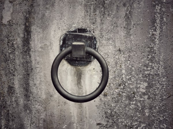 A weathered wall features a rusty metal ring affixed to it, suggesting a historical purpose. The
