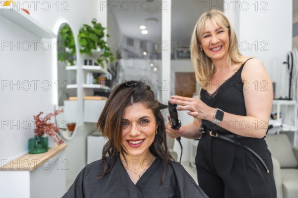 Smiling hairdresser styling hair of female customer with a curling iron in a modern, vibrant hair
