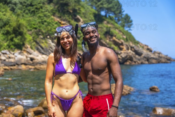 Interracial couple smiling and wearing snorkeling gear at a beautiful beach getting ready to
