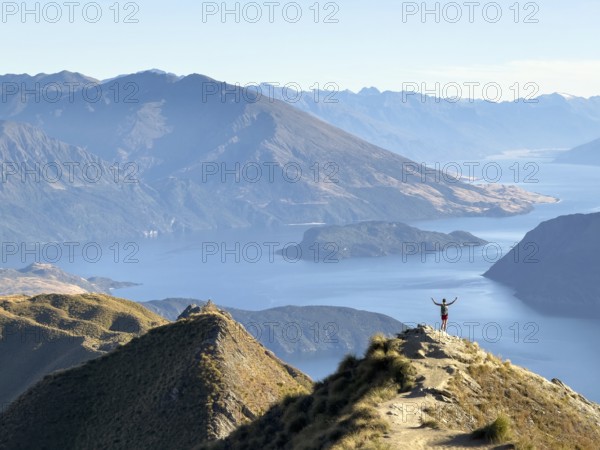 Person with outstretched arms on the hiking trail to Roys Peak Lookout, Lake Wanaka, Wanaka, South