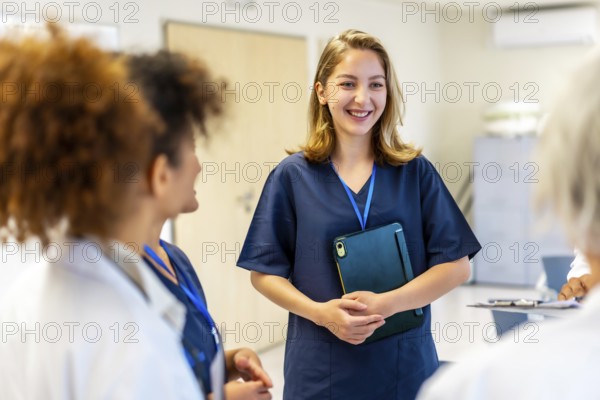 Happy nurse holding a tablet and smiling while engaging in a briefing with the medical team in a