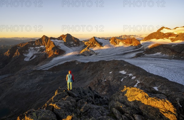 Mountaineer in front of picturesque high mountain landscape at sunrise with alpenglow, glacier and