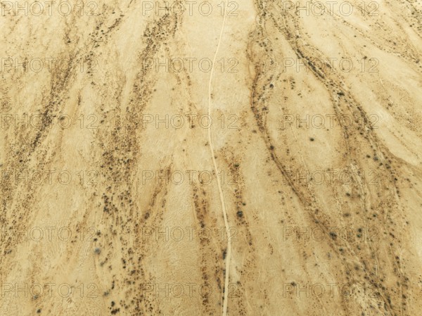 Track crossing an arid desert plain and dried-up river beds with sparse vegetation. Aerial view.