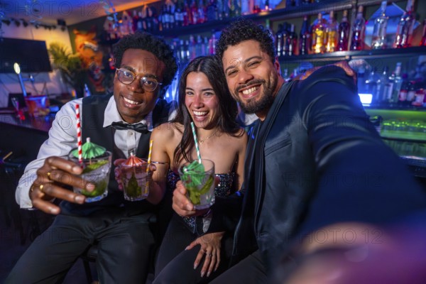 Three friends smiling and capturing a selfie while enjoying colorful cocktails at a lively bar,