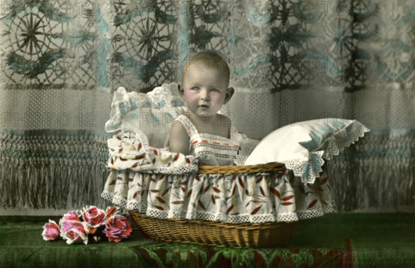 Baby in a basket, 1920s, A toddler sits cosily in a bassinet, surrounded by floral details,