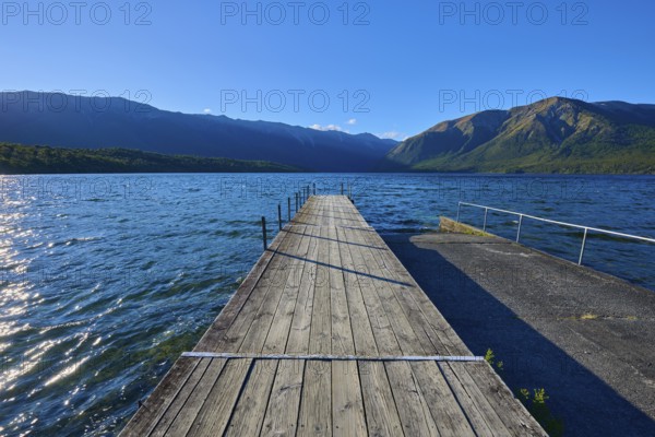 A wooden jetty stretches into a clear blue lake surrounded by majestic mountains, Summer, Lake