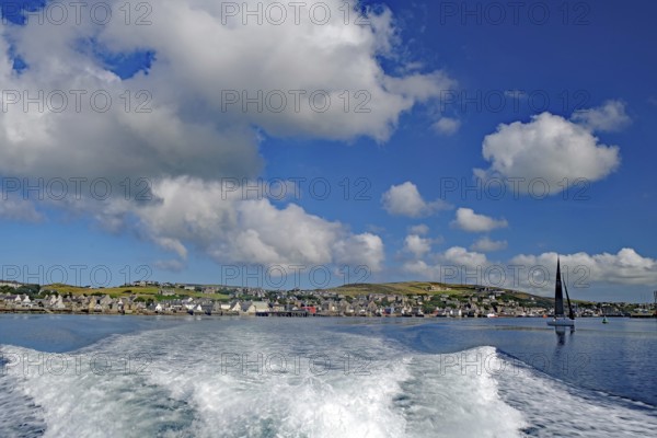 View of the sea with wave foam and boats in front of a town under a blue sky, Stromness, Mainland,