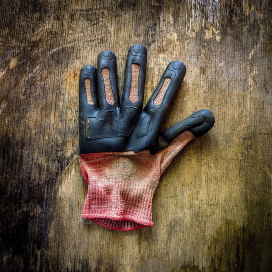 A single gardening glove lies on a rustic wooden surface, showing signs of wear and dirt from