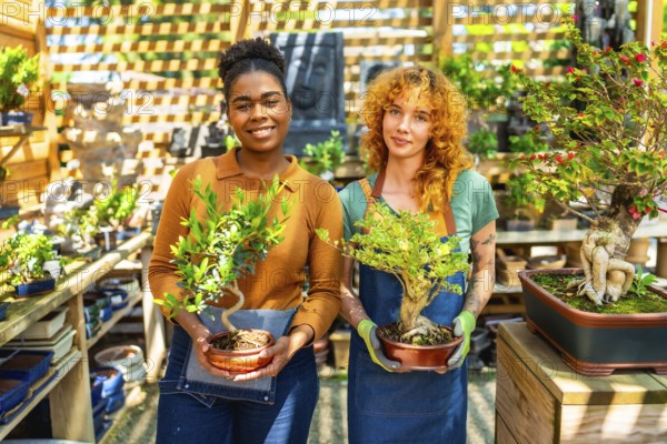 Two female gardeners holding and caring for bonsai trees while working together in a vibrant plant